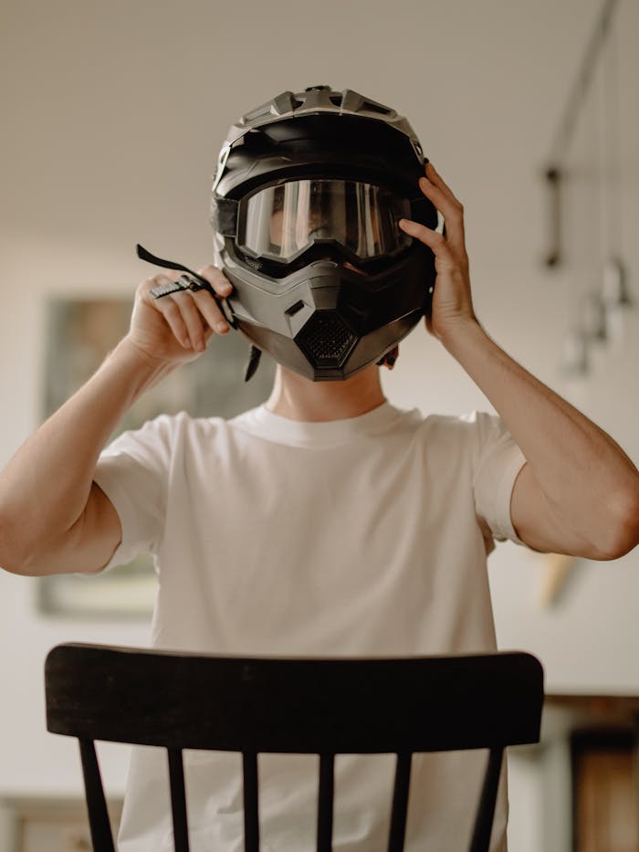 Young man in a white t-shirt holding a motorcycle helmet indoors, depicting a home setting.